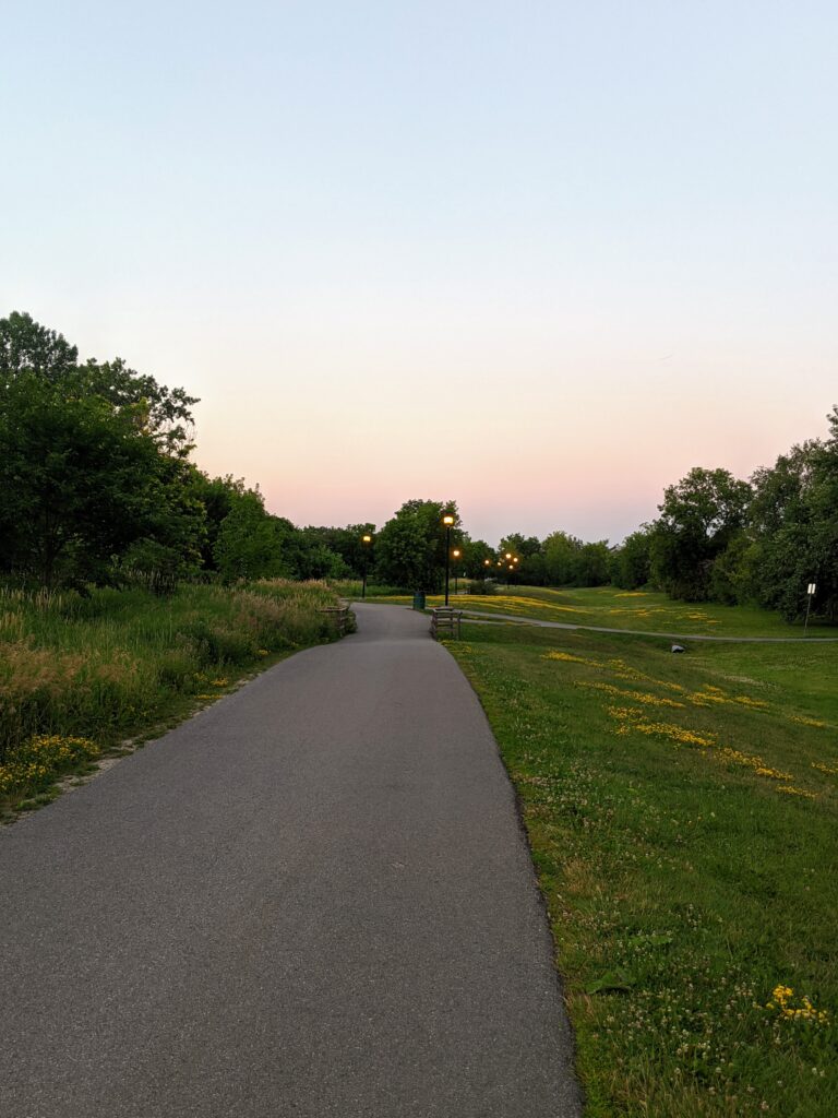 Summertime view of a section of the Greenboro Pathway with grass on either side of the wide paved path.